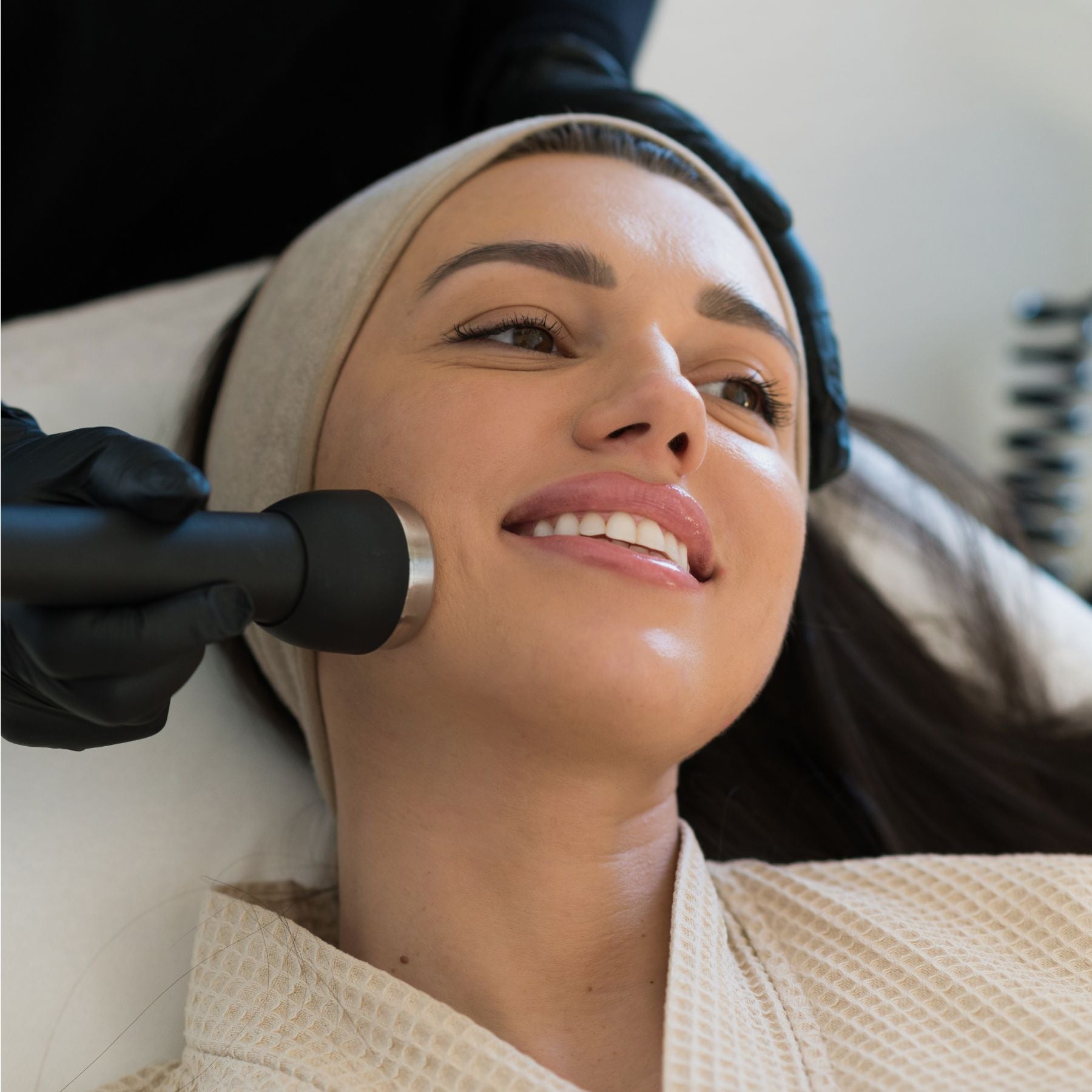 Smiling woman receiving a modern skincare treatment with a black handheld device.